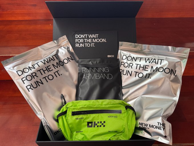 An OKX promotional gift box containing silver pouches with the text 'DON'T WAIT FOR THE MOON. RUN TO IT.', a running armband, and a neon green waist pack labeled 'OKX TRUSTED SECURE VERIFIED'.