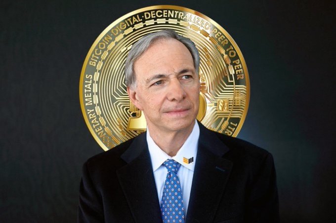 A man in a dark suit and blue patterned tie stands in front of a large golden Bitcoin coin. The coin displays text including 'BITCOIN DIGITAL DECENTRALIZED PEER TO PEER' and 'VIRES IN NUMERIS'.