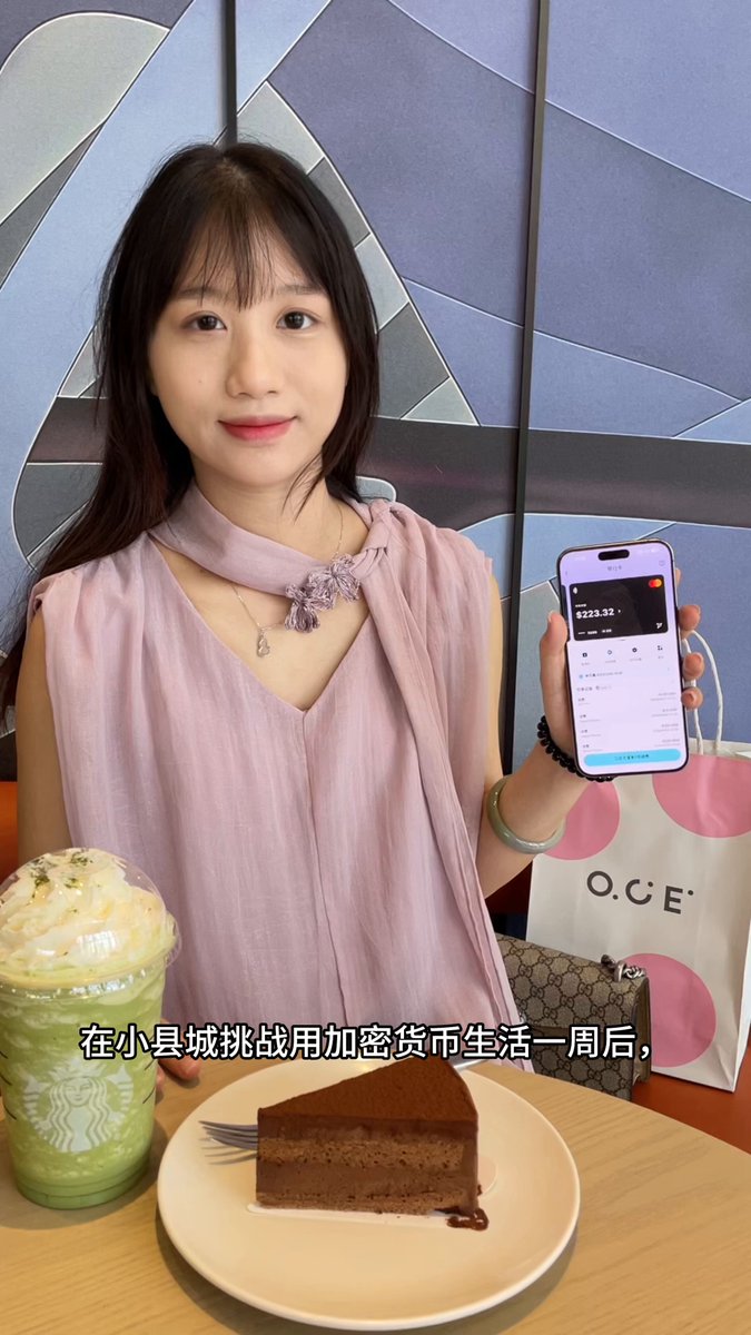 The image features a woman holding up her phone, which displays an OCE app. She is sitting at a table with a plate of cake next to her. The background includes a blue wall adorned with a painting or poster. There are also two cups on the table - one green and one white.