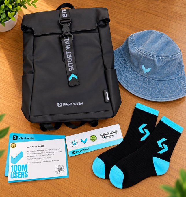 A Bitget Wallet merchandise bundle featuring a black backpack, denim bucket hat, teal and black socks, and '100M USERS' and 'Everyday Finance Optional' cards arranged on a wooden surface.