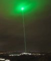 A green laser beam pierces the night sky above a cityscape, symbolizing the post's prediction of a "green light" toward a final Bitcoin shakeout and subsequent recovery cycle.