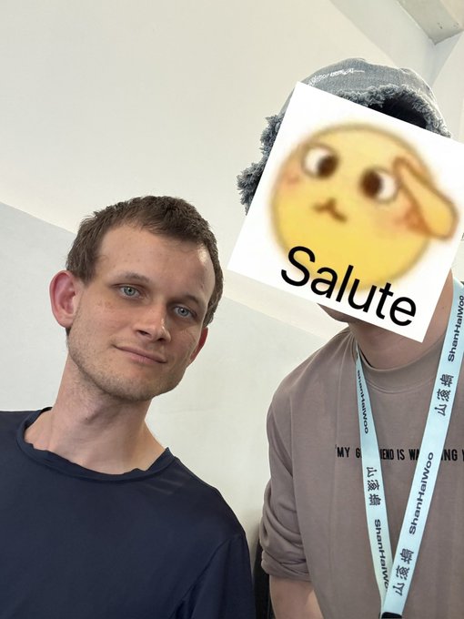 The image features two men standing next to each other, with one of them wearing a hat that has an "S" on it. The man without the hat is holding up a sign that says "Salute", which appears to be a greeting or a message of appreciation.