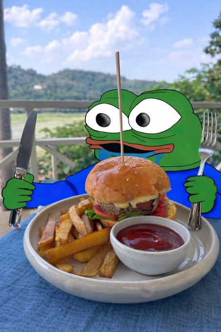 A plate of food featuring a burger, french fries, and ketchup with an edited cartoon Pepe the Frog figure holding a knife and fork on either side of the meal, set against a scenic outdoor background.