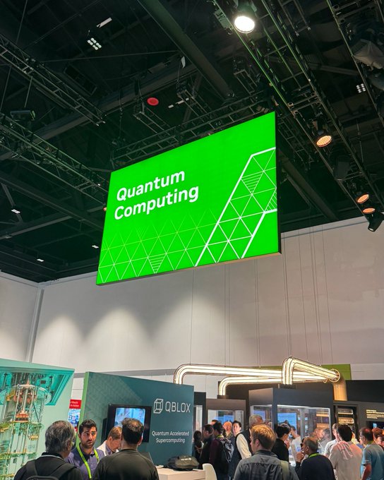 A convention hall photograph showing a large green screen displaying 'Quantum Computing' above a 'QBLOX' booth with attendees.