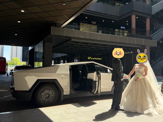 A bride in a white wedding dress and a groom in a black suit standing next to a white Tesla Cybertruck with its doors open, outside the 'L7 BY LOTTE HOTEL' building, both with cartoon emoji faces covering their heads.