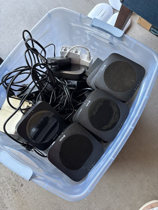 A clear plastic bin contains tangled black cables, power adapters, and several square Ring brand devices.