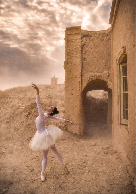 A ballerina in a white tutu strikes a graceful pose en pointe against the backdrop of ancient earthen ruins, under a dramatic cloudy sky, embodying the fusion of classical ballet with the timeless, weathered architecture of Persian heritage.