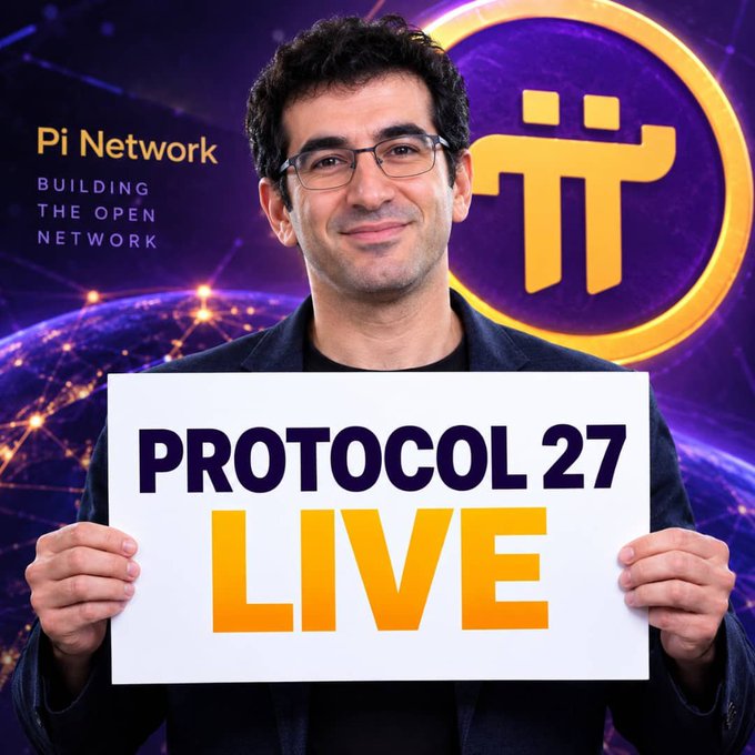 A smiling man with dark curly hair and glasses holds up a white sign reading "PROTOCOL 27 LIVE" in bold black and yellow letters, standing in front of a vibrant purple cosmic backdrop featuring a network globe, the Pi Network logo with its distinctive yellow symbol, and the text "Pi Network — BUILDING THE OPEN NETWORK," visually announcing the launch of Pi Network's Protocol 27 update mentioned in the post.