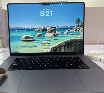A MacBook is displayed open on a desk, its lock screen showing the time "8:21" on Saturday, June 15, with a scenic lake landscape wallpaper, symbolizing the poster's pride in being able to afford a new MacBook through consistent effort in web3.