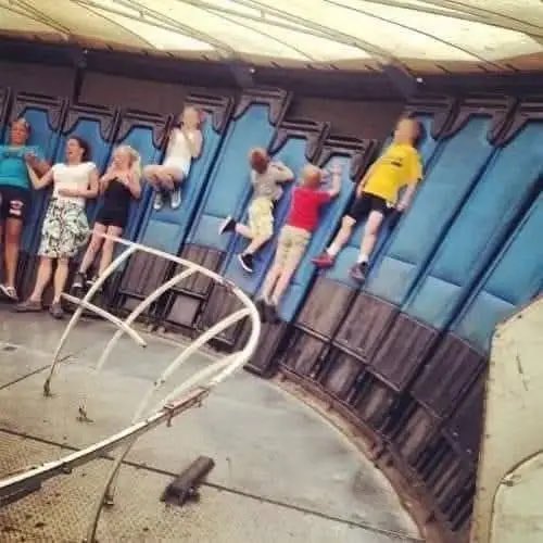 Surreal optical illusion meme showing several people lying on their backs along a curved blue structure, appearing to defy gravity.
