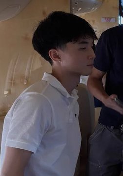 A young man in a white polo shirt stands in profile indoors, with another person partially visible behind him. The image accompanies a post reporting that “$KIMCHI” has fallen over 50% to a $13.2M market cap, but no token name or figures are visibly shown in the photo itself.