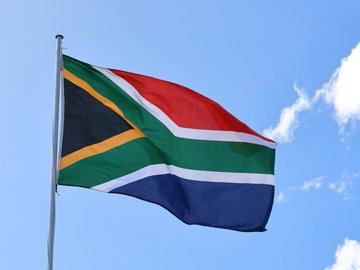 The South African flag waves against a blue sky, symbolizing the country at the center of recent proposed tax guidance from its revenue authority that would treat crypto trades, swaps, and spending as taxable disposal events under existing income and capital gains tax rules.