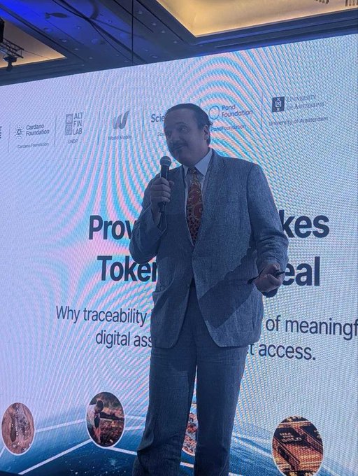 A man in a gray suit speaks into a microphone while standing in front of a presentation screen titled "Provenance Makes Tokenization Real" with various foundation logos at the top.