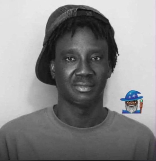 A black-and-white portrait of a man wearing a backwards cap and t-shirt, with a small cartoon wizard sticker in the corner.