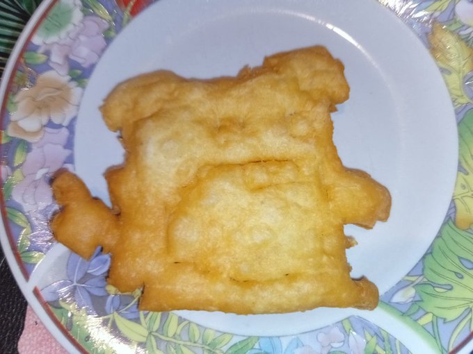 A piece of fried dough or pastry with an unusual shape resembling a figure, served on a decorative floral plate.