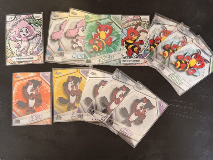 A collection of colorful trading cards featuring cartoon animals like "POLAR POODLE," "HORNET," and "HORSE" is spread across a dark surface.