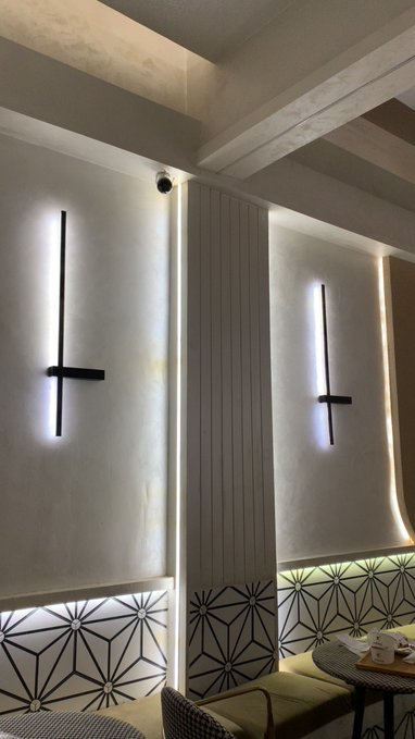 An interior space featuring minimalist wall sconces with black vertical and horizontal accents, textured walls, and a lower section with geometric patterned tile.