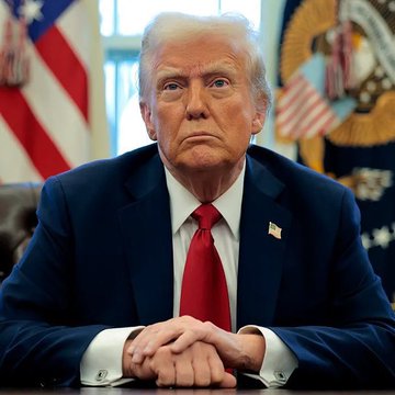 President Donald Trump sits with hands clasped on a desk in the Oval Office, with the American flag and presidential seal visible behind him. The image accompanies reporting on his Friday meeting with advisers regarding the contested ethics provisions of the CLARITY Act, ahead of the Senate's upcoming procedural vote.