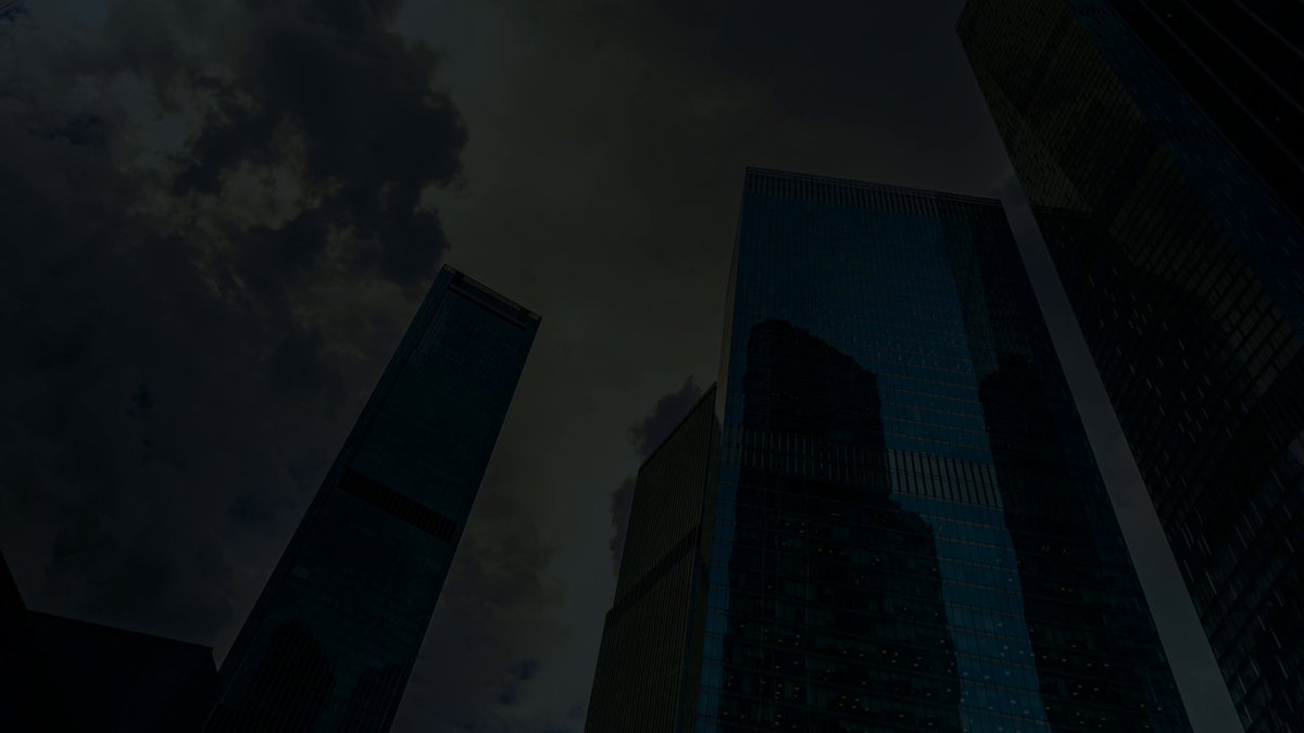 The image features a city skyline with tall buildings, including skyscrapers that are illuminated against a dark sky. The scene captures the essence of a cloudy day as the sun shines through the clouds, creating an atmospheric effect. The perspective of the photo is from below, looking up at the towering structures and emphasizing their height and grandeur. This image seems to be related to Bitcoin or cryptocurrency, as it features a prominent Bitcoiner in the post.