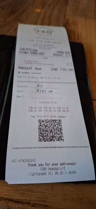 The image shows a receipt from the Fig and Bean Cafe in Hoedspruit, South Africa, which has been scanned by a QR code reader app. The app displays that the user has just paid for their lunch with Bitcoin. The text on the receipt also mentions that the payment was made using Bitcoin.