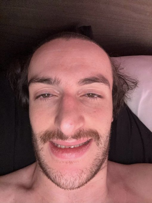 A smiling, clean-cut man with a mustache and short beard takes a close-up selfie, likely lying down, serving as a friendly face for his "$100 $SOL giveaway" post aimed at New Yorkers and Gamdom users. His cheerful expression matches the welcoming tone of his morning message and crypto promotion.
