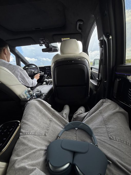 A passenger relaxes in the backseat of a vehicle with a driver at the wheel, with what appears to be AirPods Max headphones resting on their lap. The image suggests a morning commute, complementing the post's "Good morning" greeting to active community members.