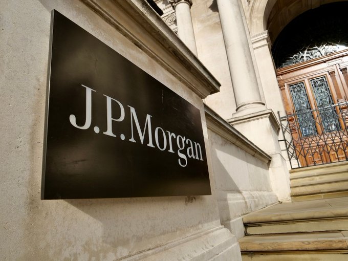 A sign displaying "J.P. Morgan" is mounted on the exterior of a building. This image relates to the post by highlighting JPMorgan's prominent role in financial commentary, particularly concerning market structure legislation and its impact on the crypto outlook.