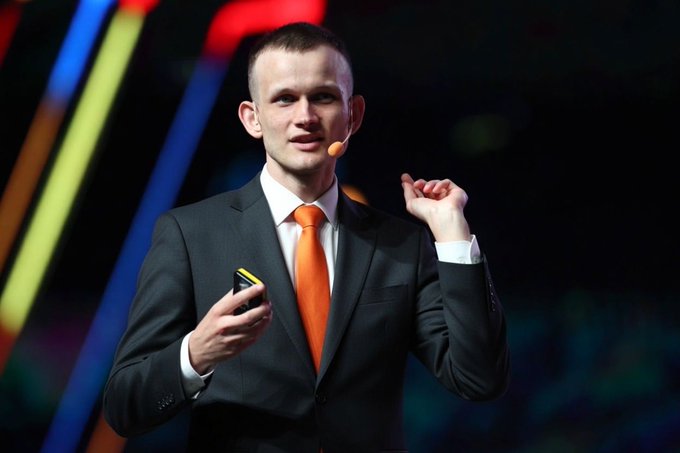 The image features a man dressed in a suit and tie standing on stage with his hands raised above his head while holding a cell phone. The background of the image shows colorful lights, which could be interpreted as neon signs or stage lighting. The caption provided suggests that this scene is related to Bitcoin maximalism, where people were called out for printing tokens and selling them for Bitcoin.