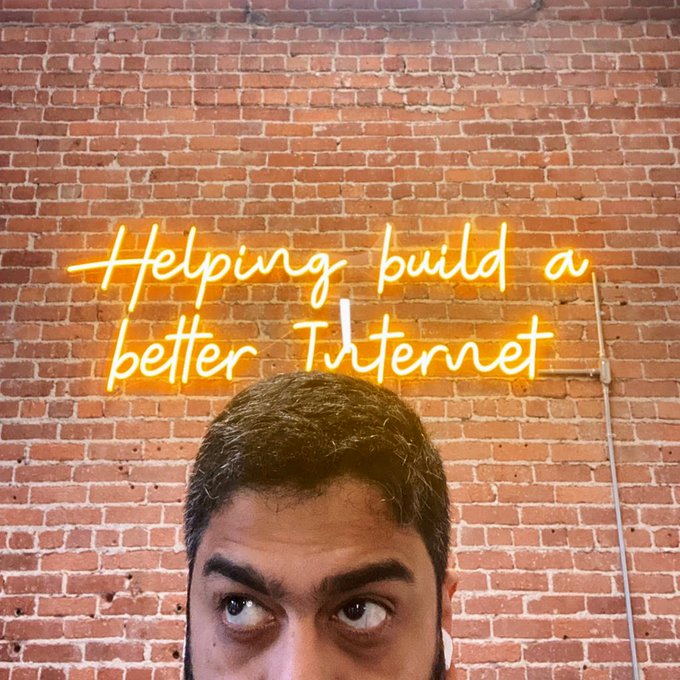A man stands in front of a brick wall featuring a glowing orange neon sign that reads "Helping build a better Internet," visually echoing the post's enthusiasm for investing more in Cloudflare ($NET).