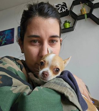 A woman with dark hair holds a small tan and white chihuahua close to her face, both looking at the camera with a calm, affectionate expression. The cozy selfie, paired with a "GM" (good morning) message, sets a warm and personal tone for the day's greeting.