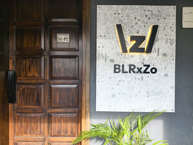 An office entrance with a dark wooden door next to a sign reading '/z/ BLRxZo' on a patterned background.