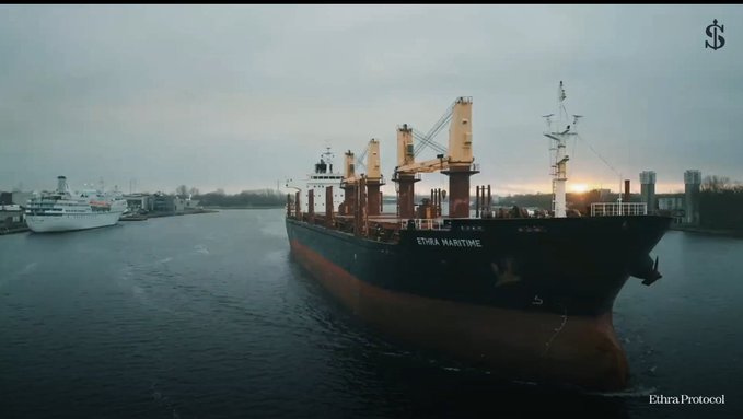 A large cargo ship named 'ETHRA WARTIME' navigates through a waterway at sunset, with another vessel visible in the background and an 'Ethra Protocol' watermark in the corner.