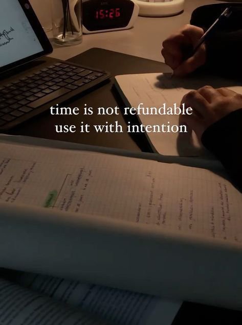A dimly lit desk scene showing hands writing in a notebook next to a laptop, with a digital clock displaying 15:26 and overlaid text reading 'time is not refundable / use it with intention.'