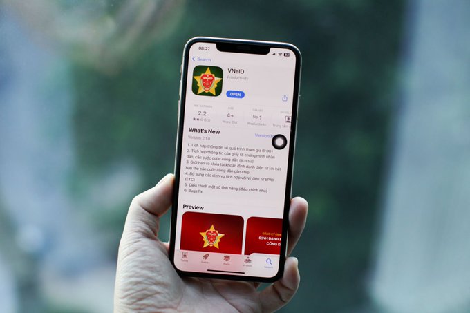 A hand holds a smartphone displaying the VNeID app, showing a 4+ rating, "OPEN" status, and version 2.1.0 with an update available, directly illustrating the Vietnamese digital identity platform that the decree requires to be linked with social media, securities, and telecommunications accounts by the end of 2026.