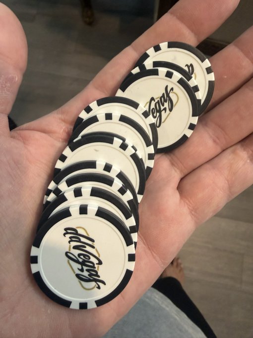 A hand holding a stack of casino-style poker chips with black and white striped edges and the signature "Ishp" printed on them in cursive.