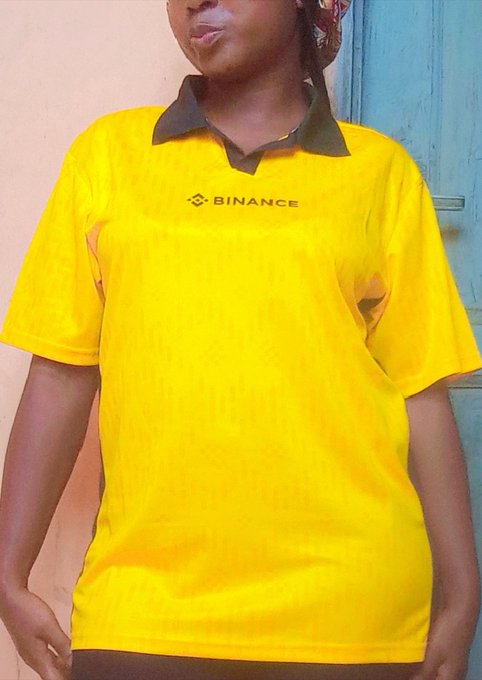 A person wearing a yellow polo shirt with a black collar and the 'BINANCE' logo on the chest.