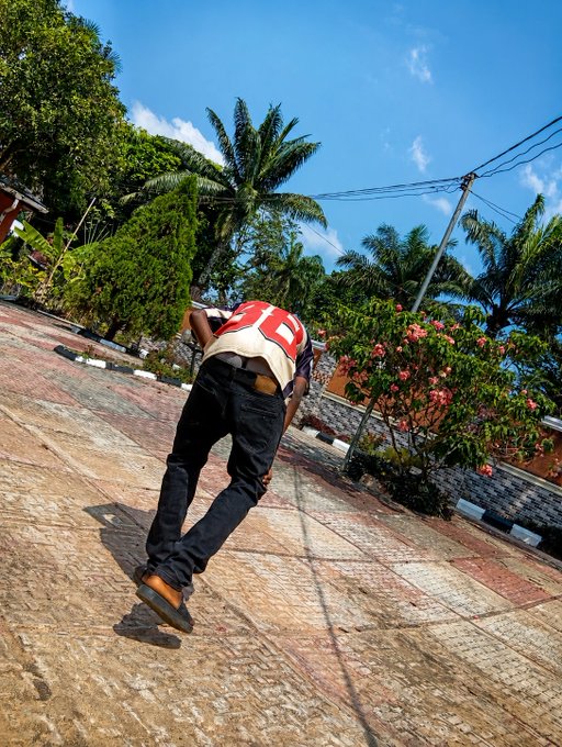 A person in a red and white jersey with the number 10 bends over on a paved street, with palm trees and flowering bushes in the background.