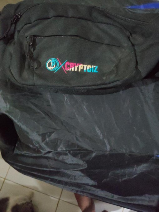 A black backpack with a colorful 'CRYPTOiZ' logo and a blue circular emblem, resting on a plastic surface.