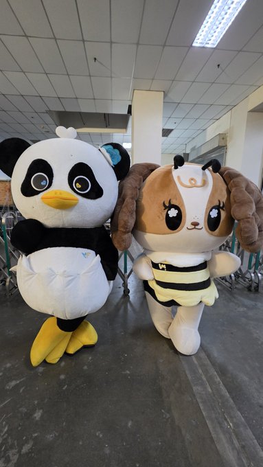 Two large mascot costumes stand side by side in what appears to be a school hallway or institutional building—a black-and-white penguin or chick character on the left and a brown dog character wearing a bee costume on the right. There is no visible text, numbers, or names in the image that would relate to the post about "Luna" or the number "55252526252525."