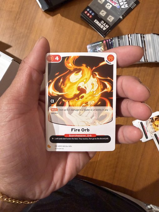 A hand holding a 'Fire Orb' spell card (value 4) with a fire creature artwork, featuring abilities 'Deal up to 5 damage to a leader or an entity in any Gauntlet' and 'Sear' keyword.