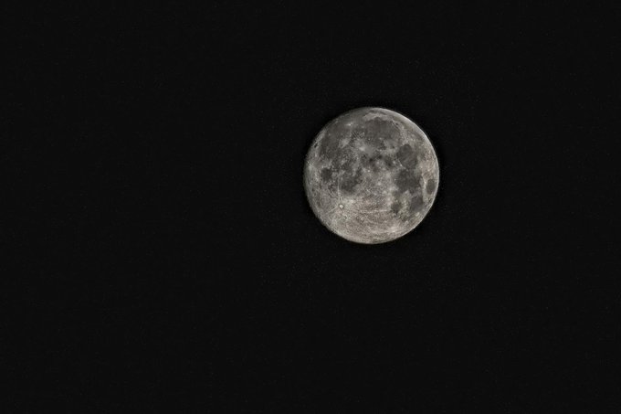 A detailed grayscale photograph of a full moon centered against a pitch-black night sky.