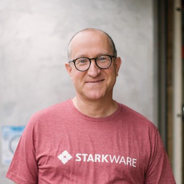 Eli Ben-Sasson, co-founder of StarkWare, stands smiling in a red "STARKWARE" branded t-shirt and glasses. The image accompanies his warning that Ethereum's slow roadmap could allow it to be overtaken by a more modern and better blockchain competitor.