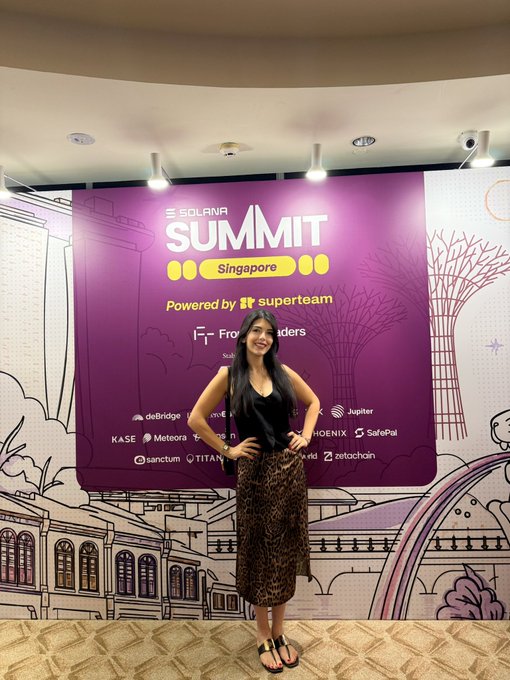 A smiling woman in a black top and leopard-print skirt poses confidently in front of a vibrant purple "Solana Summit Singapore" backdrop, powered by Superteam. The event banner displays numerous sponsor logos including Jupiter, SafePal, Phoenix, KASE, Meteora, Sanctum, Titan, ZetaChain, and Frontier, reflecting the post's excitement about the summit and Frontier Traders.