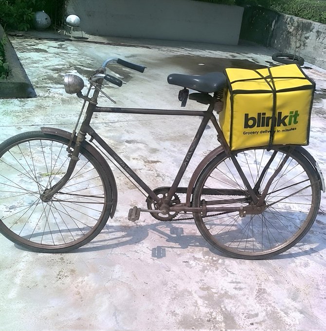 A rusty old bicycle is parked on a concrete surface, fitted with a bright yellow 'blinkit – Grocery delivered in 10 minutes' delivery box on its rear rack.