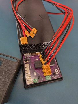 An open black electronic device (appears to be a cryptocurrency miner) with red and black power cables connected via XT60 connectors, showing internal circuitry.