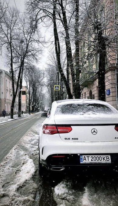 A white Mercedes-Benz GLE 400 with Ukrainian license plate "AT 2000 KB" is parked on a snowy city street lined with bare trees and classical buildings. The image showcases a luxury vehicle, fitting the "G M X family" lifestyle theme referenced in the post, while the snowy urban setting adds a scenic backdrop.