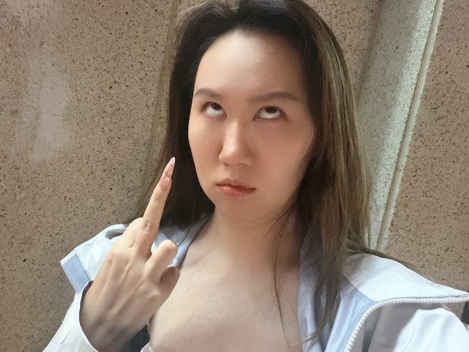 A woman with an exaggerated wide-eyed expression points at her temple in frustration, perfectly matching her rant about repeatedly missing a token (gcat) because the project kept changing their profile picture—causing her to lose out on a potential 1m+ gain while she was busy preparing to go to the gym.