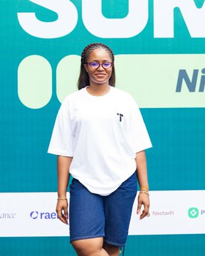 A smiling young woman wearing glasses, a white t-shirt, and denim skirt poses in front of a teal "Solana Summit" backdrop featuring sponsor logos including NectarFi. The image captures a candid attendee moment from the Solana Summit Nigeria event.