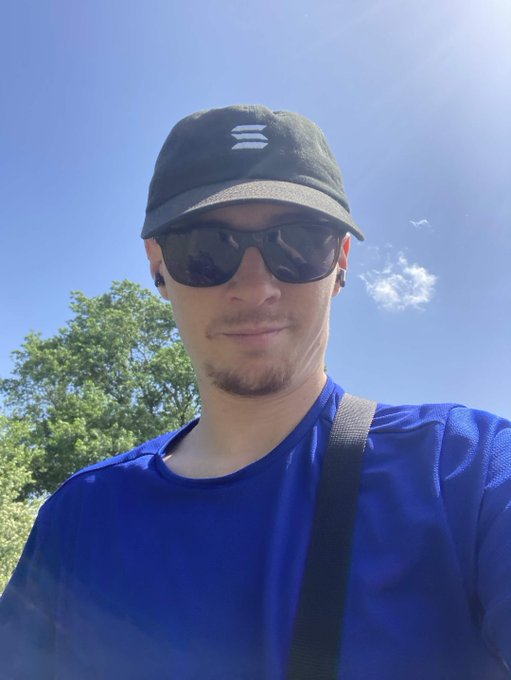 The image features a man wearing sunglasses, a blue shirt, and a black backpack with a white logo. He has a beard and appears to be smiling for the camera. The caption of the image includes a reference to the popular social media platform "Solana" and an optimistic statement about its future success.