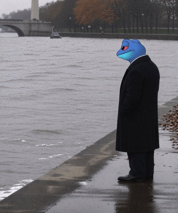 The image features a man standing near a body of water, possibly a river or lake, wearing a black coat and sunglasses. The man appears to be staring out at the water with an expression of contemplation or boredom. There are no other people visible in the scene.